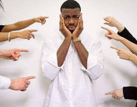 Worried man surrounded by pointing fingers, symbolizing bullying and social pressure.